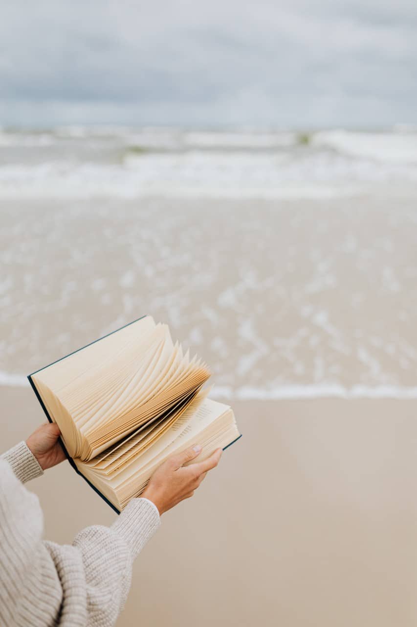 a woman on a beach holding a book about online business and entrepreneurship
